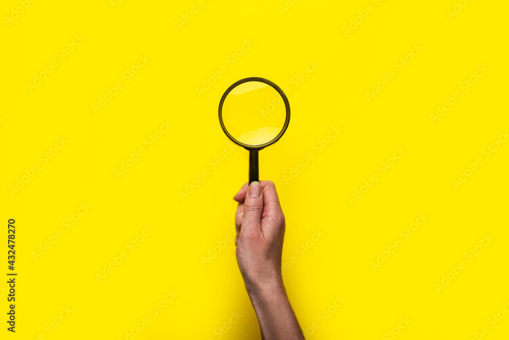 female hand holds a magnifying glass loupe on a yellow background female hand holds a magnifying glass loupe on a yellow background