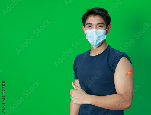 Asian young man wearing protective hygiene mask trust and confident show arms with bandage plaster after getting Coronavirus or Covid-19 vaccine injection. Idea for safe and drug allergy free