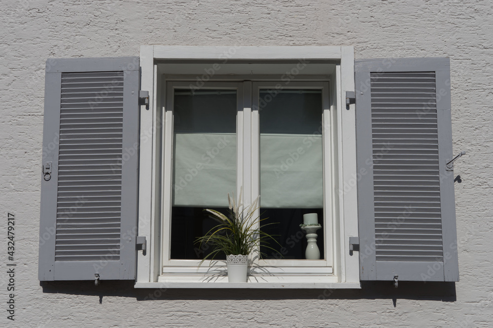 Background: old white double casement window with grey shutters in a plastered and white painted wall
