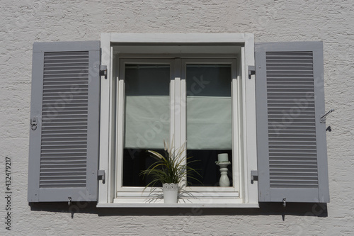 Background  old white double casement window with grey shutters in a plastered and white painted wall