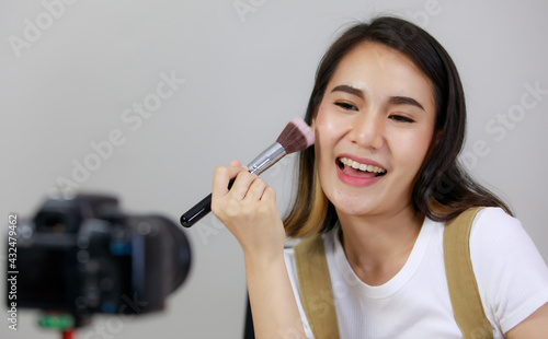 Smiling Asian young beauty blogger or Influencer show brushing make-up and recorded by using dslr camera. vlogger streaming online. Concept Selling products online.