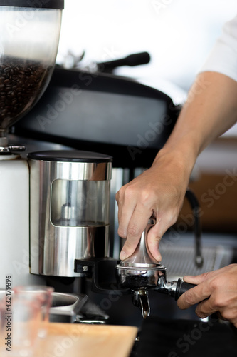 close up photo of male hands holding a metal tamper and a portafilter with coffee in a coffee shop. A man barista preparing for pressing ground coffee for brewing espresso or americano in a cafe.