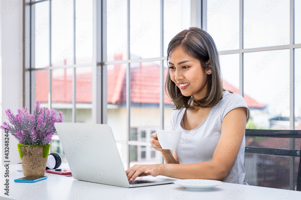 Portrait of Asian woman freelancer working at home, sitting at desk table in living room, drinking coffee Portrait of Asian woman freelancer working at home, sitting at desk table in living room, drinking coffee