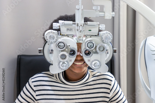 African young woman girl doing eye test checking examination in clinic or optical shop, sitting at phoropter equipment. Eyecare concept. photo