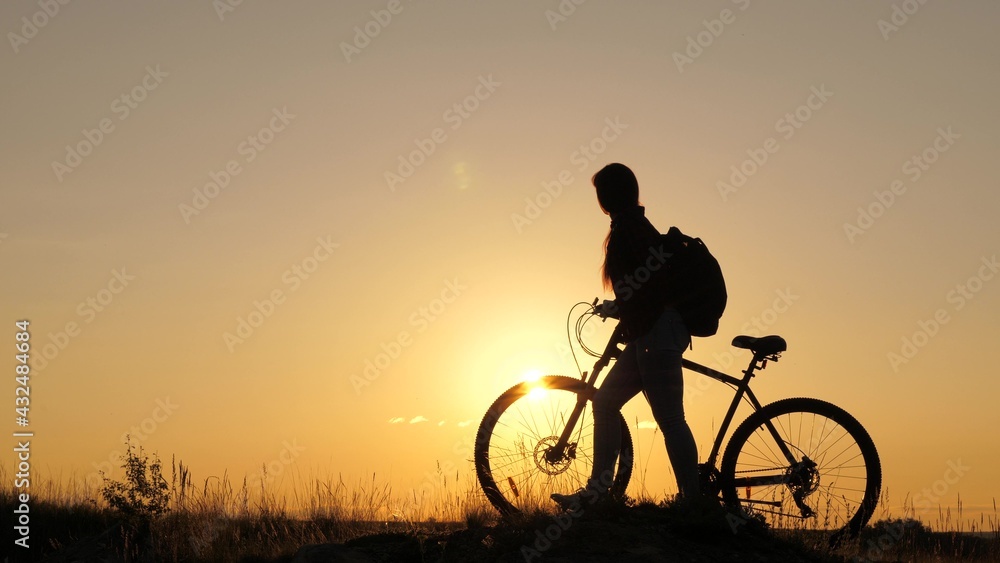 A free girl travels on a bike, rests, looks at the sunset and enjoys the sun. Adventure and travel concept. A healthy young tourist walks with bicycles across the field, enjoying nature, fresh air.