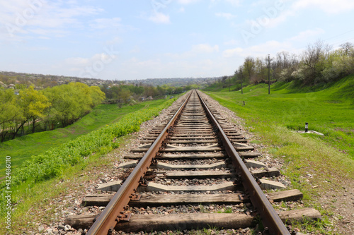 Railway on the green meadow. Rails and sleepers. Railway tracks in rural areas. Green meadows and young trees
