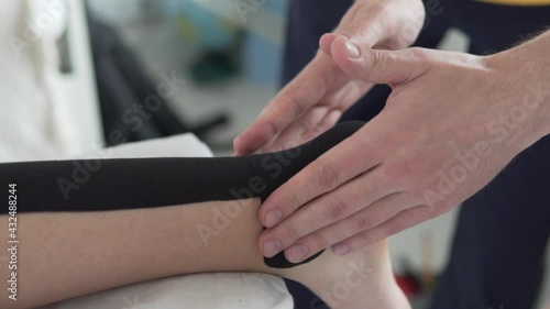 Dr. Traumatologist glues the tape on the athlete's ankle, close-up of the leg. kinesiology therapeutic tape, Kinesio tape, k-tape photo