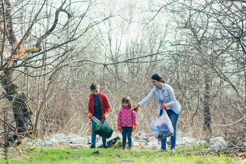Young family mother with two children volunteers clean the spring park, collect garbage and plastic bottles, spend time together, learn to take care of the environment and take care of it