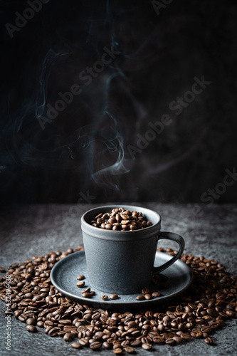 Gray cup full of steaming coffee beans on a dark gray stone background