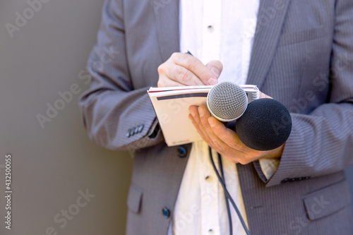 Journalist at media event or news conference, holding microphone, writing notes. Broadcast journalism concept. photo