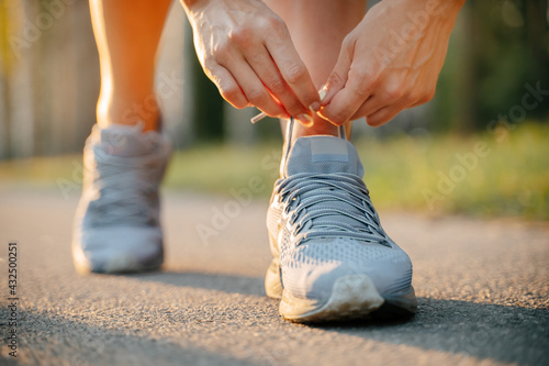 Close-up of hand tying shoelaces ready to run on the road.Gray sports sneakers on the background of the road.