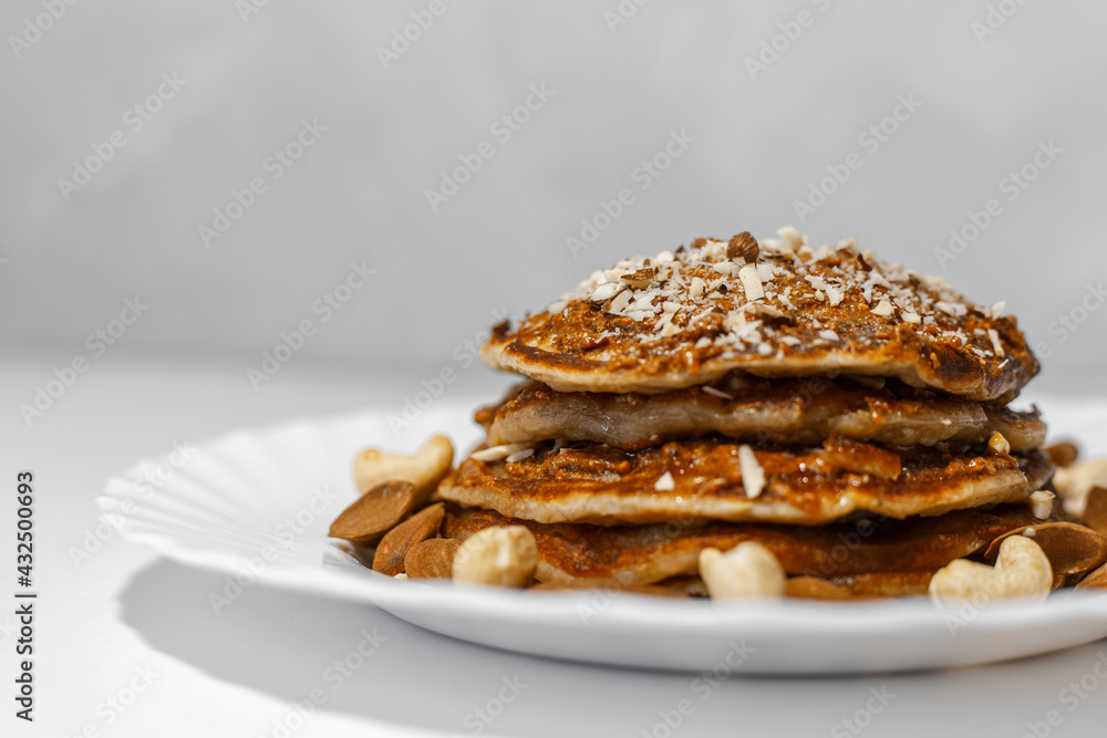 Healthy breakfast; close-up of homemade vegan pancake with raw cashew and almond nuts in white plate.