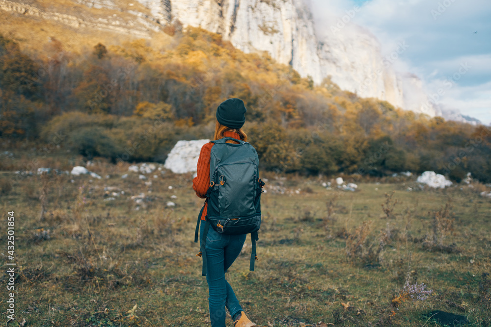 a traveler in a sweater jeans with a backpack on the back and a warm hat mountains autumn landscape
