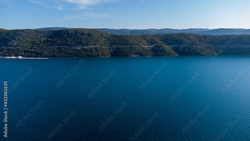 Aerial drone view of sea and peninsula in distance. Sun reflection on water surface. Adriatic sea and Klek peninsula near city of Neum, Bosnia and Herzegovina. Aerial drone view of sea and peninsula in distance. Sun reflection on water surface. Adriatic sea and Klek peninsula near city of Neum, Bosnia and Herzegovina.