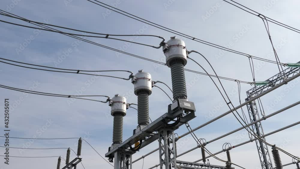 Glass and ceramic insulators with connecting wires at distribution substation under blue sky with light clouds close view Glass and ceramic insulators with connecting wires at distribution substation under blue sky with light clouds close view