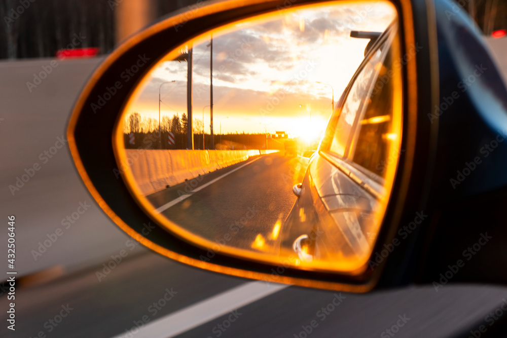 Rear view car mirror view back to nature on evening with sunset. Sunset reflected in the mirror of the car road car and landscape