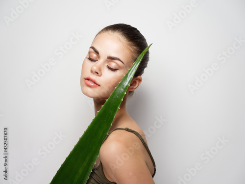 beautiful woman with aloe leaf near face on light background cropped view 