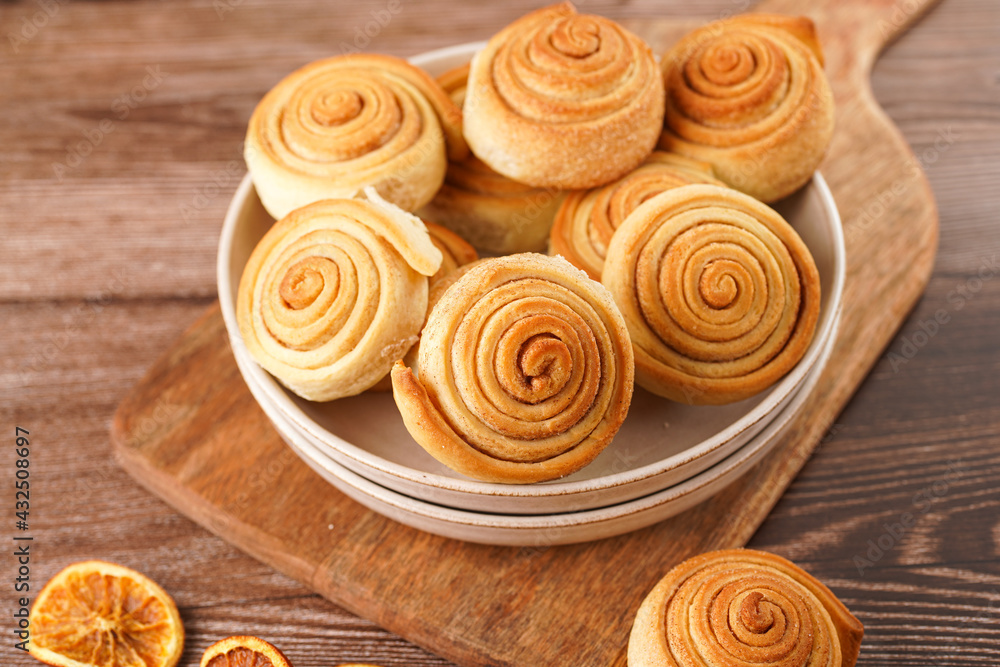 Fototapeta premium Several cinnamon buns in a beige bowl on wooden board on wooden table