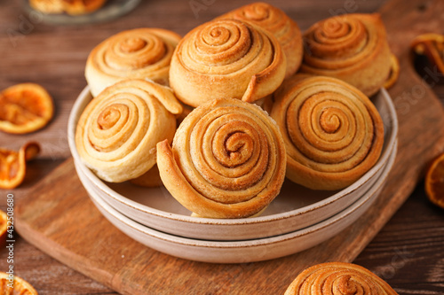 Several cinnamon buns in a beige bowl on wooden board on wooden table