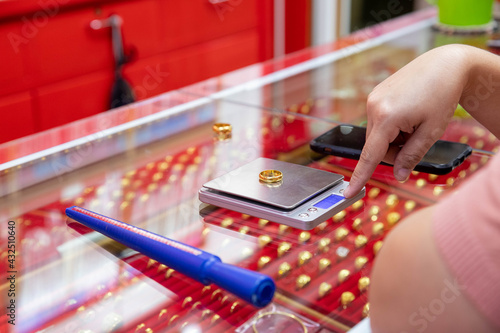 The gold shop employee is weighing the gold ring. To check for customers