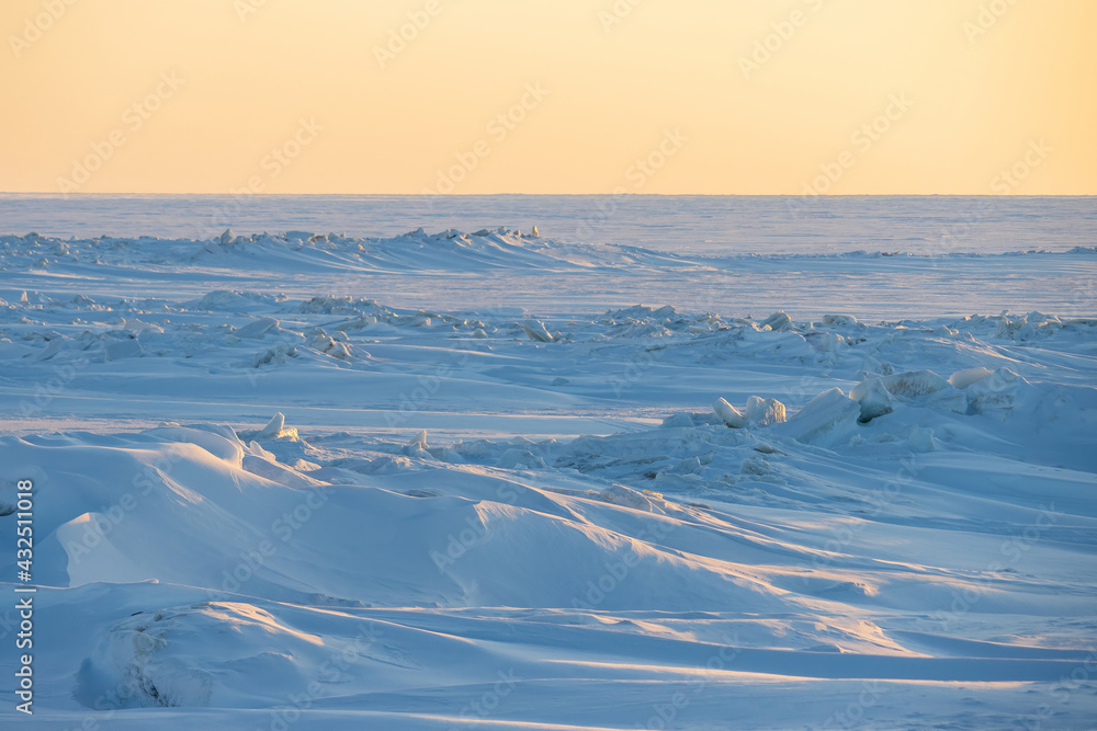 Obraz premium Winter arctic landscape. View of snow and ice at sunset. Ice hummocks on the frozen sea in the Arctic. Cold frosty winter weather. Harsh polar climate. Travel and hikes to the far north to the Arctic.