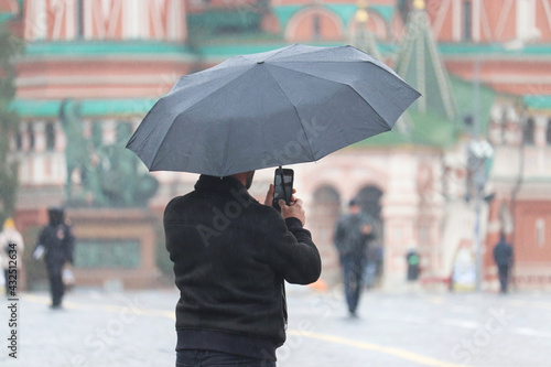 Man with umbrella taking photos on the Red Square in Moscow during rain on background of St. Basil s Cathedral