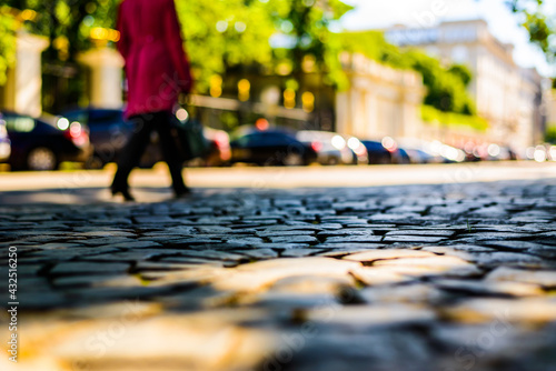 Summer in the city, woman in a red coat walking down the street with a paved stone near the park. Close up view from the level of paving stones