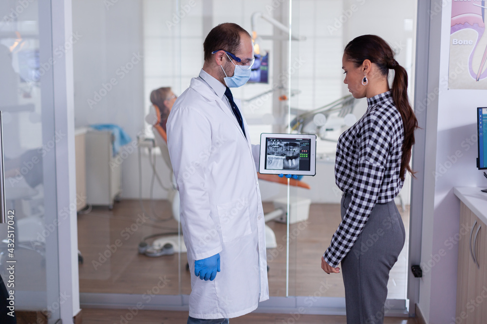 Dentist with face mask showing patient dental x-ray in stomatology specialist reception. Explaining diagnosis during appointment, senior man sitting in dental chair. Dentist with face mask showing patient dental x-ray in stomatology specialist reception. Explaining diagnosis during appointment, senior man sitting in dental chair.