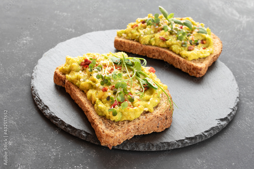 Two toasts with avocado, microgreens and hemp seeds on a black slate board Two toasts with avocado, microgreens and hemp seeds on a black slate board