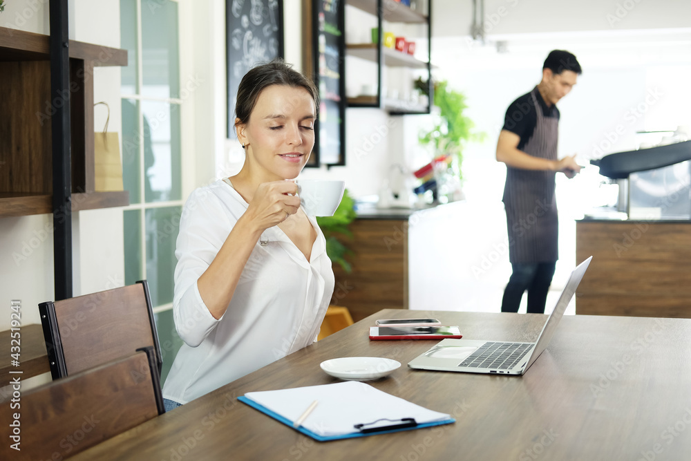Smiling Caucasian woman happy with a cup of hot coffee in the morning with sunrise at cafe. She is relaxing with tablet in cafe at office. Lifestyle of businesswoman and technology concept Smiling Caucasian woman happy with a cup of hot coffee in the morning with sunrise at cafe. She is relaxing with tablet in cafe at office. Lifestyle of businesswoman and technology concept