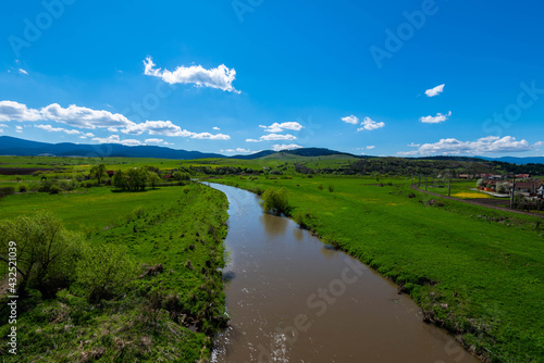 Calm flowing Olt river , vibrant green fields at spring, blue sky with white clouds.