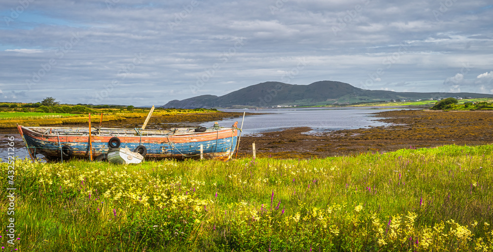 Large lagoon or marsh after ebb tide with old rusty, ruined paddle boat and mountain range in the background in Ring of Kerry, Ireland