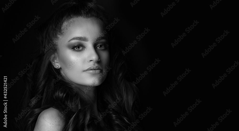 Monochrome portrait of an alluring young woman posing at the black background