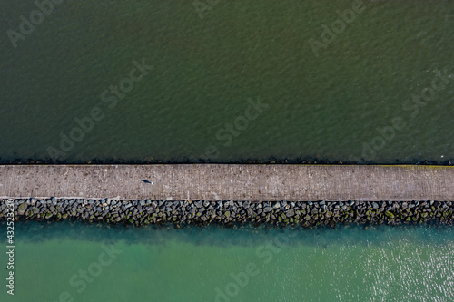 Tablou canvas An aerial shot of a person walking on the great south wall  walk towards Poolbeg Lighthouse in Dublin, Ireland
