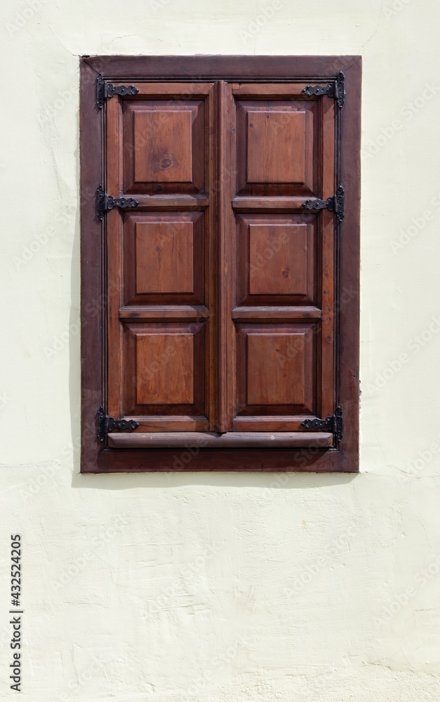Aged red wooden closed window on white old plastered wall close-up. Rustic house style. Aged red wooden closed window on white old plastered wall close-up. Rustic house style.