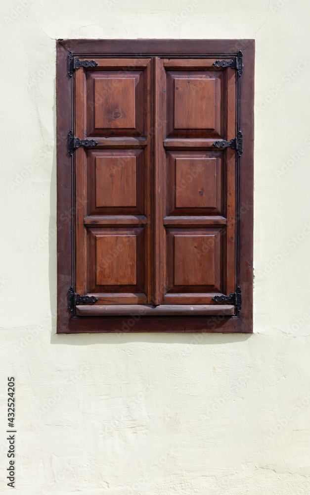 Aged red wooden closed window on white old plastered wall close-up. Rustic house style.