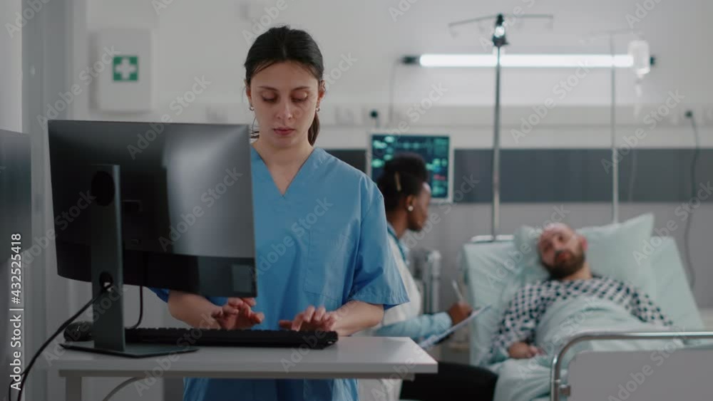 Front view of nurse typing medical expertise on computer while in background black practitioner doctor discussing with sick man healthcare treatment. Hospitalized patient having respiratory disorder Front view of nurse typing medical expertise on computer while in background black practitioner doctor discussing with sick man healthcare treatment. Hospitalized patient having respiratory disorder