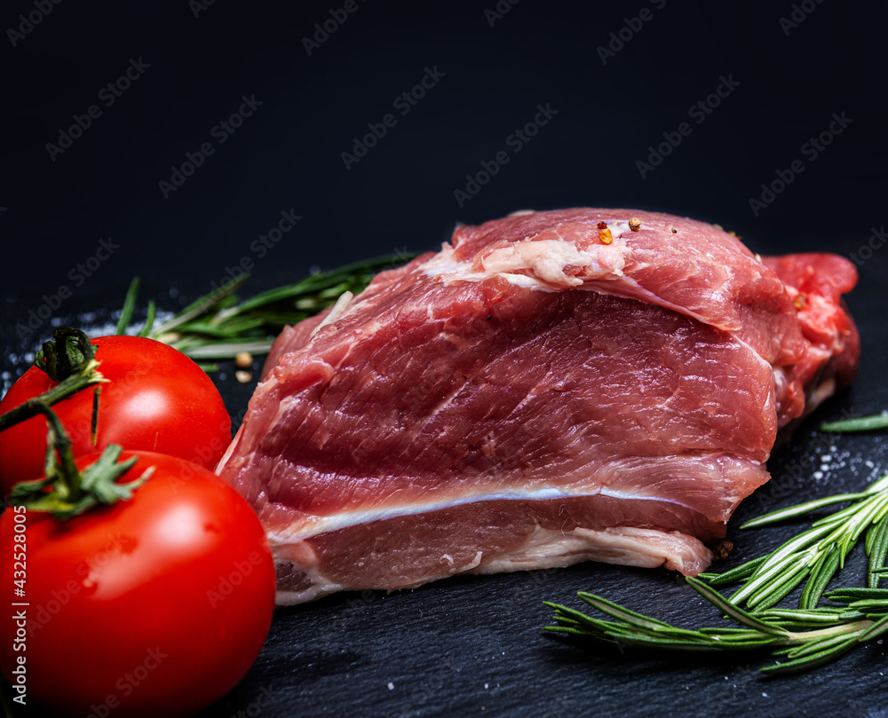 Fresh pork meat with ingredients for cooking on dark background. Tomato and rosemary
