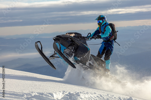 snowmobile. a guy rides a snow bike in the mountains against the backdrop of a ridge of rocks and a snow-covered valley. prof snowmobiler stands on a track with snow swirls.