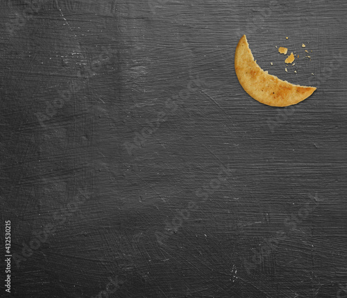 Bite of a cookie biscuit in a half-moon shape. Eid Greetings concept. Moon-shaped cookie - creative idea. isolated on black texture background photo