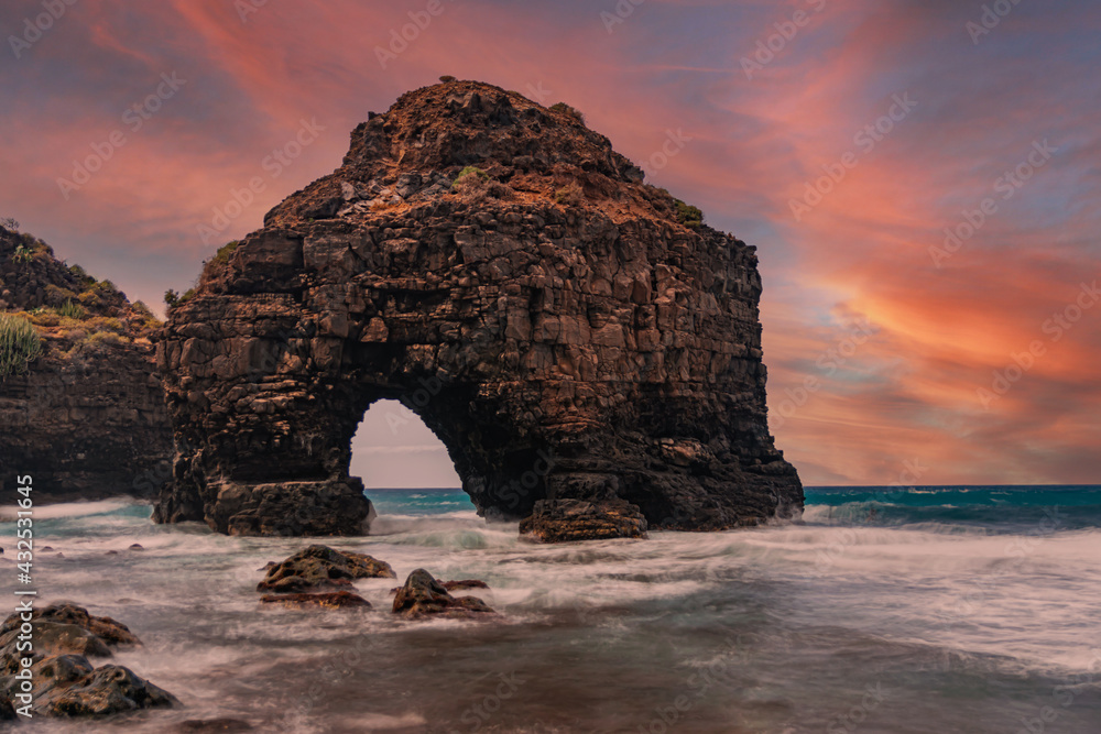 Volcanic rock arch, Los Roques beach, sky with clouds and sunset light, long exposure, Los Realejos, Tenerife, Canary islands