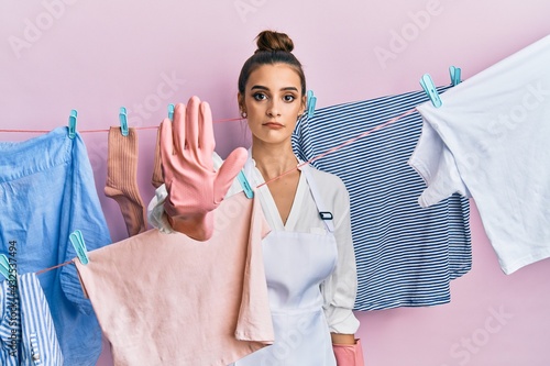 Beautiful brunette young woman washing clothes at clothesline doing stop sing with palm of the hand. warning expression with negative and serious gesture on the face.