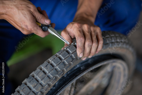 A motorbike mechanic is trying to use a device to remove the metal from the tire that caused the tire to puncture.