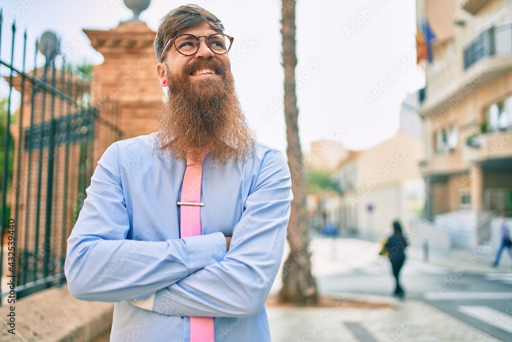 Young redhead businessman with crossed arms smiling happy  at the city.