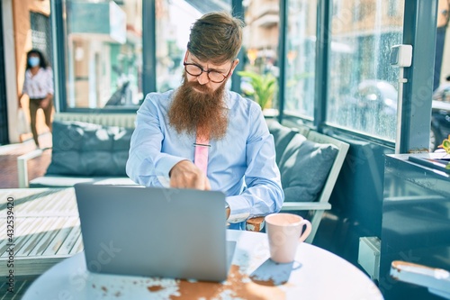 Young redhead businessman doing video call using laptop at coffee shop terrace. Free Download Young redhead businessman doing video call using laptop at coffee shop terrace. - GFXLoad