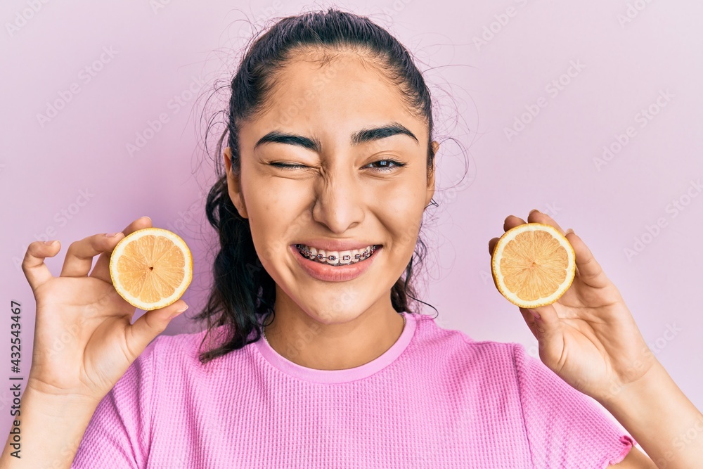 © Krakenimages.com - Hispanic teenager girl with dental braces holding lemon winking looking at the camera with sexy expression, cheerful and happy face.