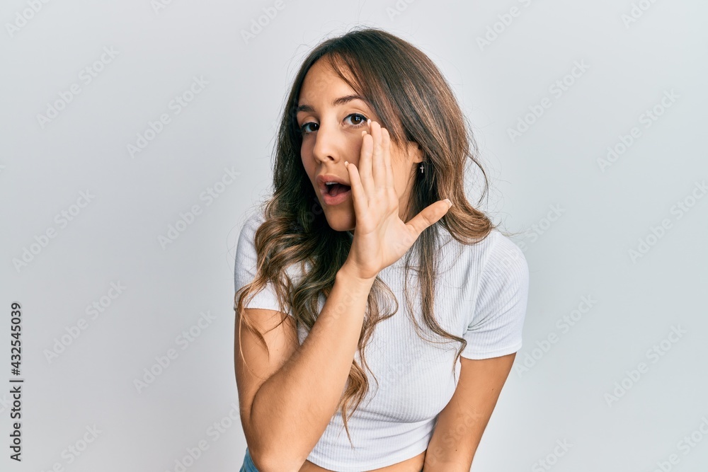 Young brunette woman wearing casual white t shirt hand on mouth telling secret rumor, whispering malicious talk conversation Young brunette woman wearing casual white t shirt hand on mouth telling secret rumor, whispering malicious talk conversation