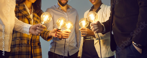 Background with young multiethnic business team holding glowing vintage Edison lightbulbs. Multiracial men and women join shining electric light bulbs for teamwork and sharing creative ideas photo