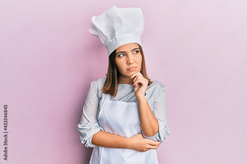 Young beautiful woman wearing professional cook uniform and hat with hand on chin thinking about question, pensive expression. smiling with thoughtful face. doubt concept. Young beautiful woman wearing professional cook uniform and hat with hand on chin thinking about question, pensive expression. smiling with thoughtful face. doubt concept.