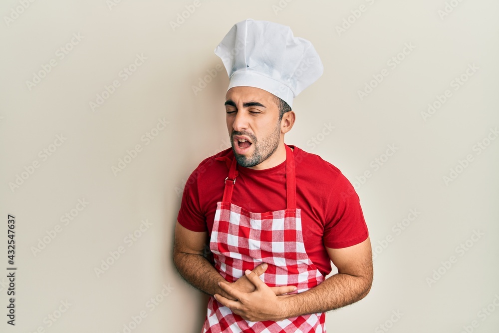 Young hispanic man wearing baker uniform with hand on stomach because nausea, painful disease feeling unwell. ache concept. Young hispanic man wearing baker uniform with hand on stomach because nausea, painful disease feeling unwell. ache concept.